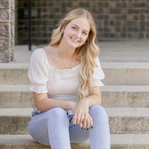 Janelle Hoback in a white shirt and blue pants, sitting on stone stairs.