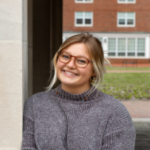 Jenna Reitz leaning against an archway, smiling and wearing a gray sweater.