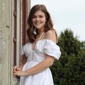 Julia Bee smiling at the camera, wearing a white off-shoulder dress.