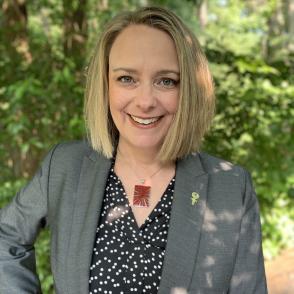 Kathy Fahl posed in a black shirt with white dots on it with a gray blazer over it.
