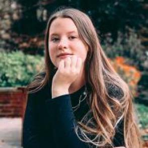 Kendra McKitrick leans forward on on hand, smiling. She wears a black long sleeve shirt.