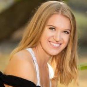 Megan Handle smiles, wearing a white tank top with an off the shoulder black top over it.