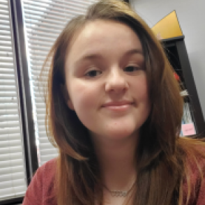 Natalie Harris smiling at the camera wearing an orange shirt.