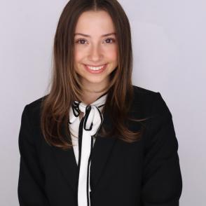 Elise Walters stands in front of a white wall, smiling. She is wearing a white ascot that has black accents along the edge.