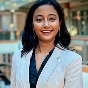 Aanya Datta smiles at the camera, wearing a dark shirt and a white blazer