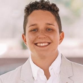 Alina Taylor smiles at the camera, wearing a white collared shirt and cream blazer