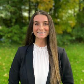 Ambrea Dellafave smiles at the camera, wearing a white ruffled blouse and a black blazer