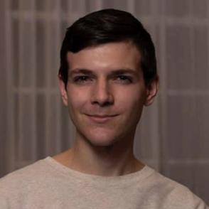 Andrew Connolly stands in front of a curtain, smiling and wearing a white shirt