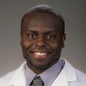Andrew Williams smiles at the camera, wearing a light purple shirt and a white coat.