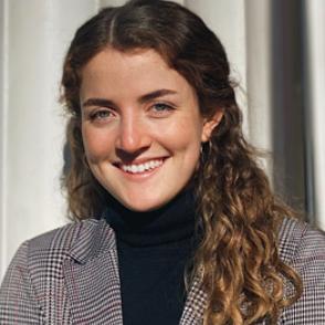Micaela Beatham-Garcia smiles at the camera, wearing a black turtleneck and black, cream, and red striped blazer