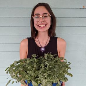 Daniela Grijalva smiles at the camera, wearing a black tank top and holding out a plant.