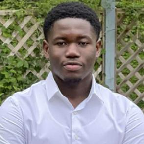 Desmond Owusu half-smiles at the camera, wearing a white collared dress shirt