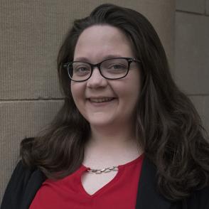 Faith Laughlin smiles at the camera, wearing glasses, a red blouse and black blazer