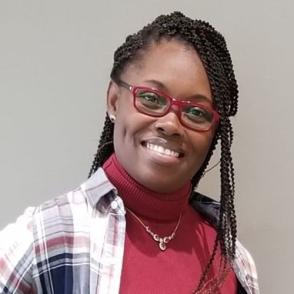 Faustina Mensah smiles at the camera, wearing red glasses and a red turtleneck wearing a flannel
