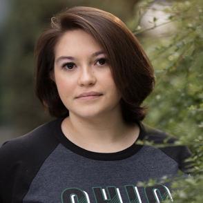 Isabel Alvarez stands outside and gives a half-smile, wearing a dark gray baseball style shirt with 'OHIO' written on it.