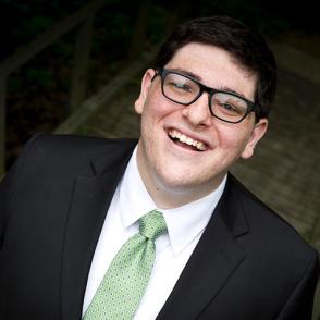 Jacob Levin smiles at the camera, wearing a suit and light green tie as well as glasses