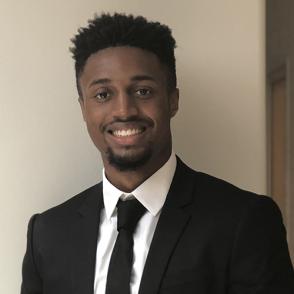 Jalen Warren smiles at the camera, wearing a black suit and tie