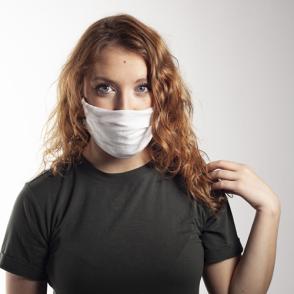 Jordan Schmitt poses in front of a white background, wearing a gray shirt and a white mask