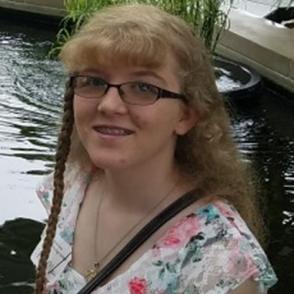 Julianna Yates smiles at the camera, wearing glasses and a pink, blue and white floral shirt