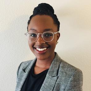 Laura Ndoigo smiles and wears a gray tweed blazer and black blouse.