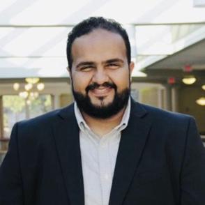 Majed Zailaee smiles and wears a dark blue blazer and white button-up shirt.