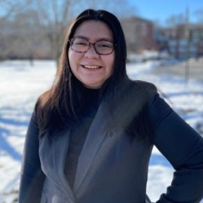Maribel Antunez-Uriostegui poses with an arm on Maribel's hip, wearing a black long sleeved shirt and gray blazer vest