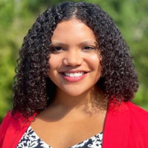 Maya Meade smiles and wears a black and white paisley pattern shirt with a bright red sweater over it