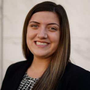 McKenzie Taylor smiles at the camera, wearing a black and white patterned shirt and black blazer