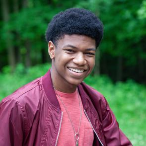 Sedric Granger smiles at the camera, wearing a red shirt and a darker red jacket.