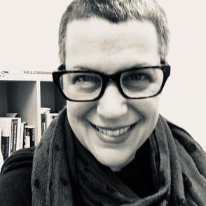 A black and white selfie of Wendy-Marie Martin smiling and wearing black glasses and a scarf.