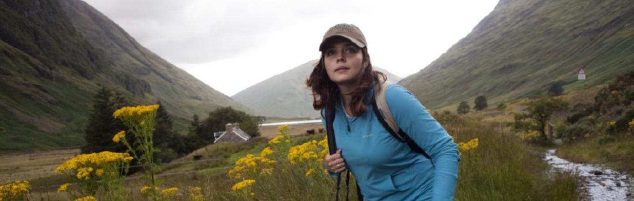 Photographer looking off into the distance as they stand in a field between two mountains. 