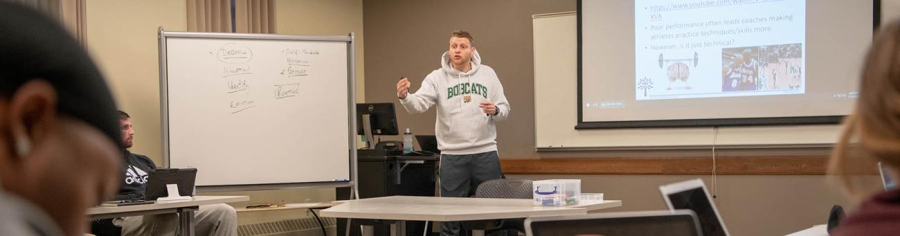 Professor points to a display screen while lecturing students in class