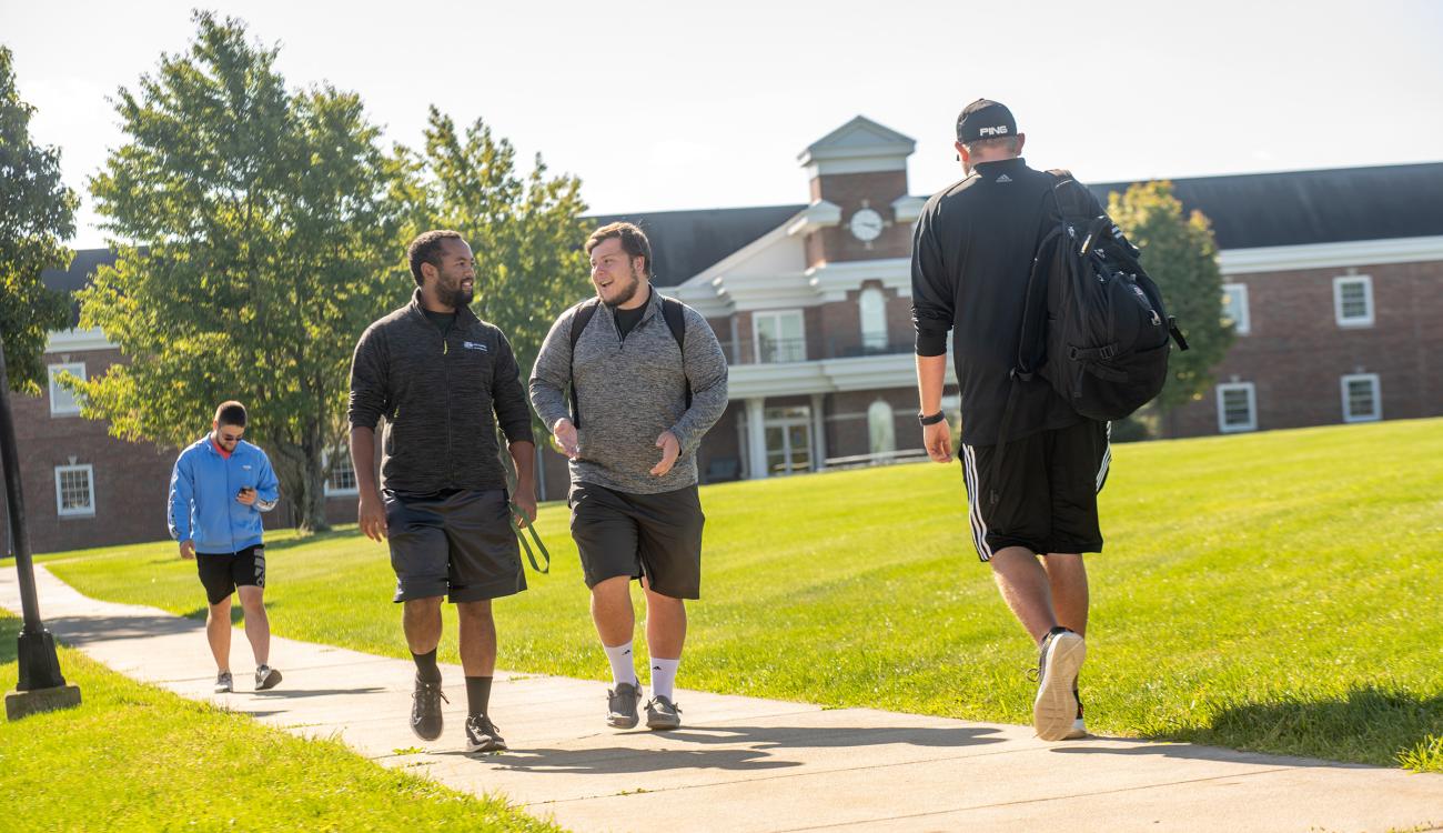 two men walk on a path talking in front of the Ohio University Eastern building