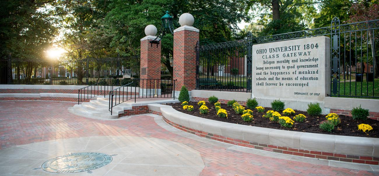 Class Gateway at Ohio University, lined with yellow flowers and a setting sun in the background