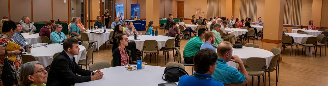 Faculty and staff sit around tables during an event.