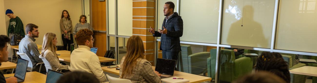 An instructor stands at the front of the class explaining a topic to students.