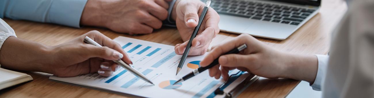 Three people holding pens point at various graphs on a piece of paper.