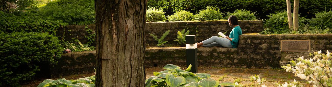 A student sits in the courtyard outside of Alden Library reading.