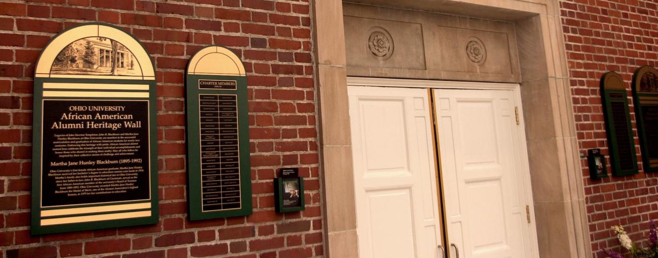 Brick wall with white doors and plaque to left with names.