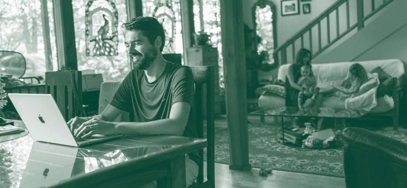 Man sitting at a laptop in a house with children behind him