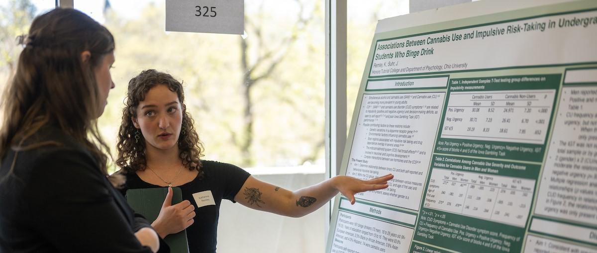 A photo of a student talking about their research with an onlooker.