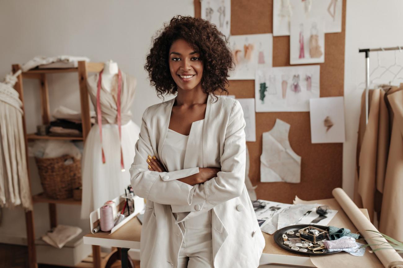 Woman leans against desk with fashion sketches on wall. Image by Freepik.