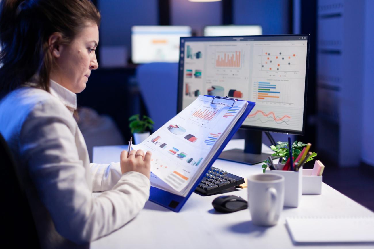 A woman compares graphics from clipboard with graphics on computer. Photo by Freepik.