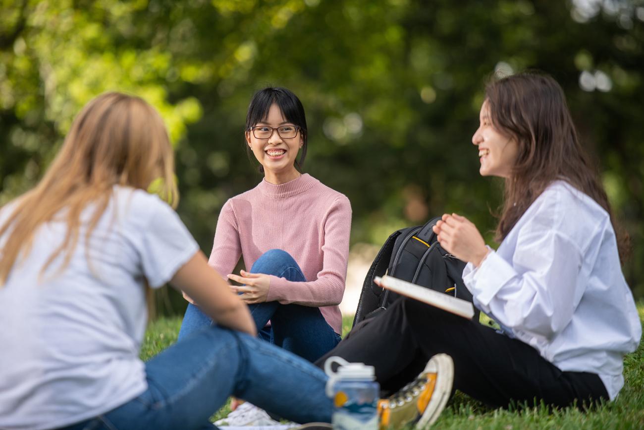 Three international students sitting on grass together.