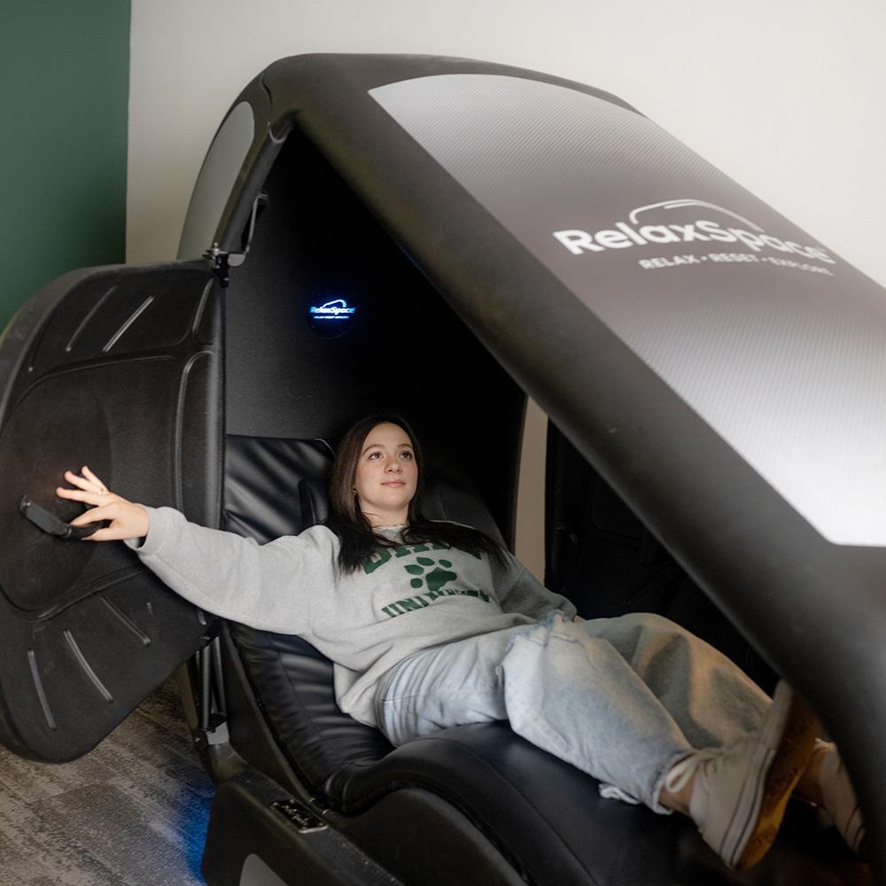Student relaxing at Ping Center in a relax space machine.