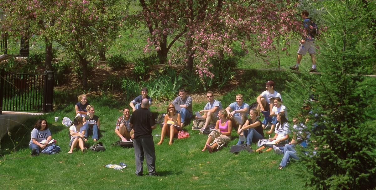 professor speaking to students outside on the lawn surrounded by spring season trees
