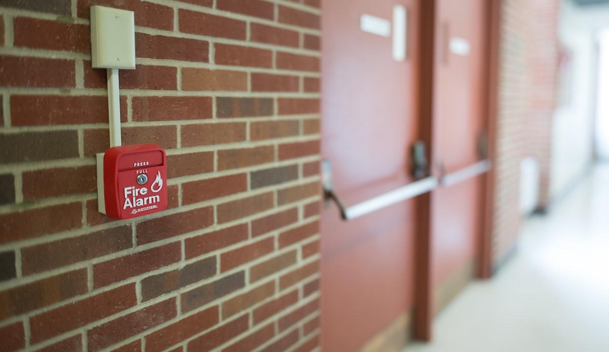 a fire alarm pull on a brick wall near two double doors