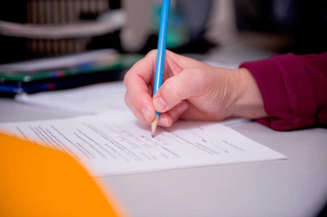 Person in a maroon shirt, holding a blue pencil, while completing a form