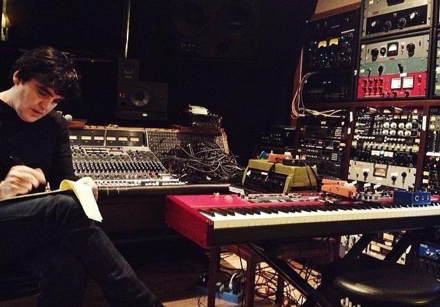 Man writing in room with sound equipment surrounding him