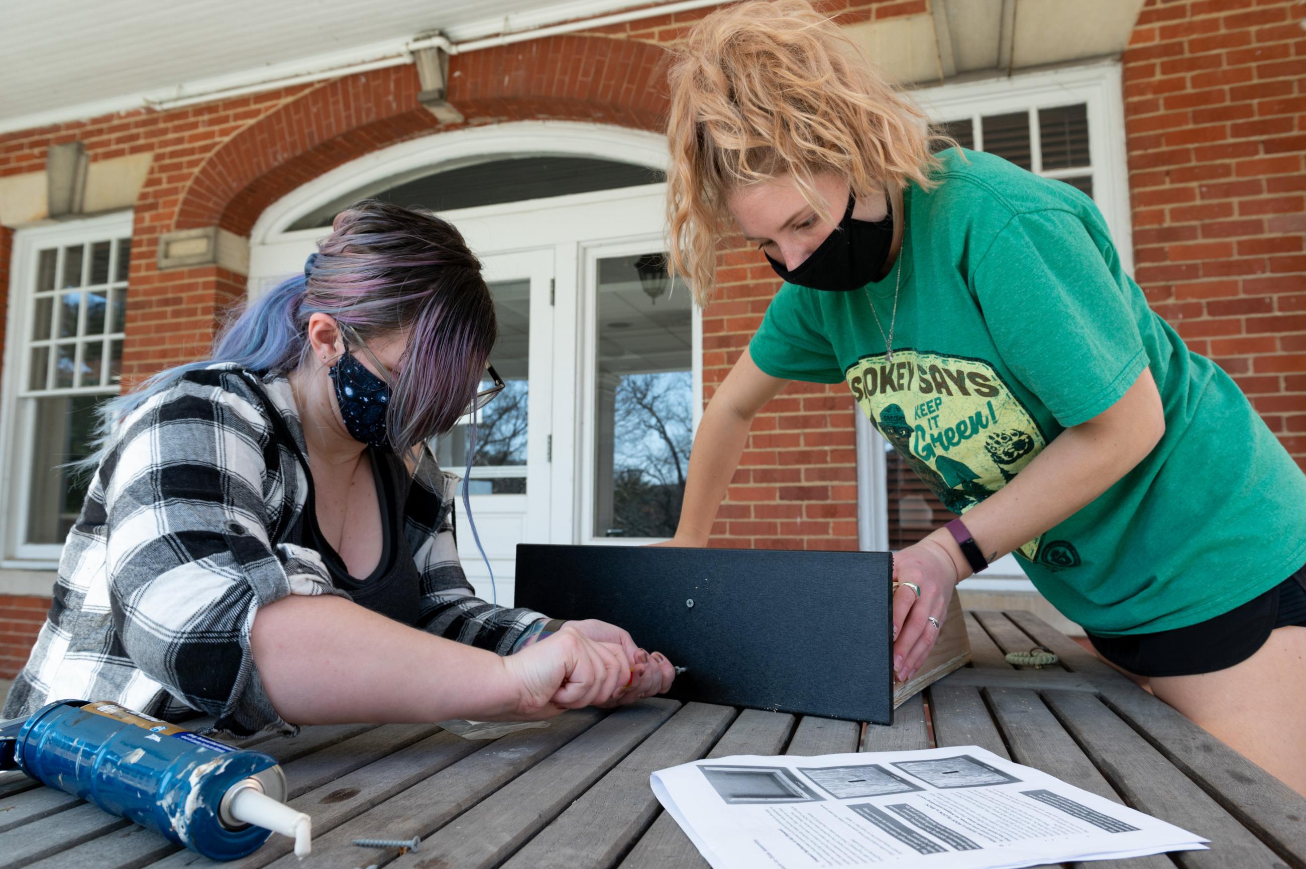 Two women work to attach a piece to a bat house as they build it.
